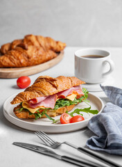 Croissant sandwich with ham, cheese, tomato  and arugula on a plate on a light background