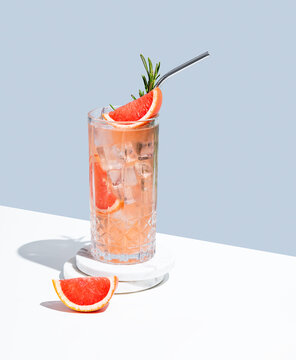 Refreshing mocktail with grapefruit, rosemary and ice in a glass on a white blue background with shadow.