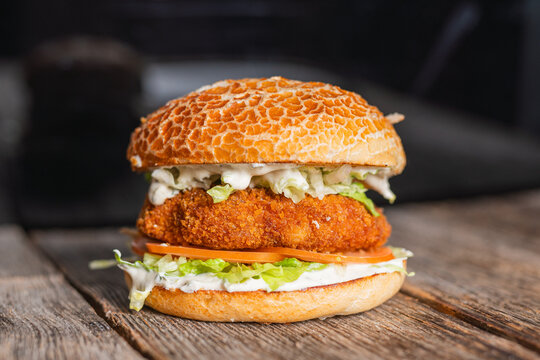 Crispy chicken burger with fresh lettuce, tomato, and a creamy sauce, served in a rustic setting on a wooden table.


