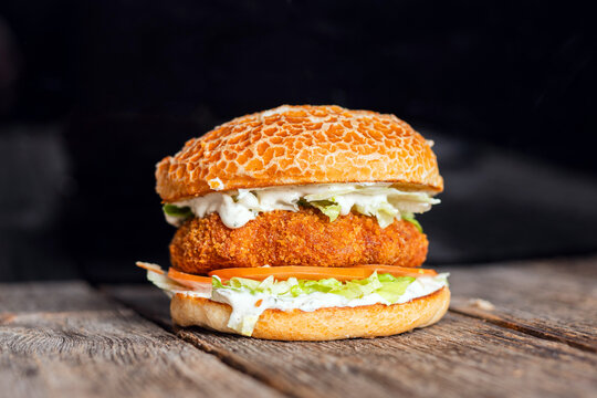 Crispy chicken burger with fresh lettuce, tomato, and a creamy sauce, served in a rustic setting on a wooden table.

