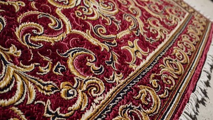 Close-up, low-angle video shot of an ornate red and gold embroidered carpet, highlighting intricate patterns and textures in a detailed view. - Powered by Adobe