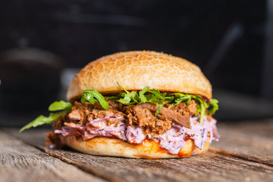 Pulled beef burger with fresh arugula, coleslaw, and barbecue sauce, served on a rustic wooden table.