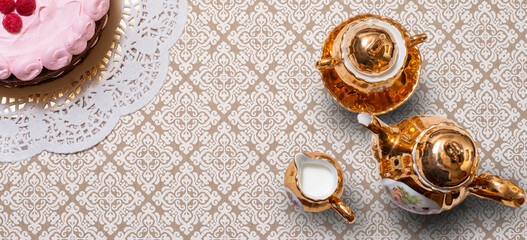  Background Aerial view of  golden tea set with a teapot, cup,milk jug and cake on a decorative patterned tablecloth