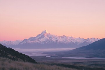 A photograph of the silhouette of mountains in the distance, with a light pink sky and a distant mountain range with snow on top.