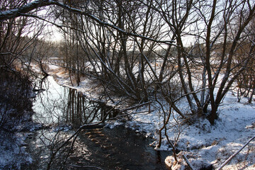 Sunny winter day. The small river under the name Maska flows in the tunnel from trees. Water flows...