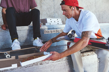 Man, skater and friends with food outdoor for pizza lunch, fitness break and bonding with takeaway. People, nutrition meal and skateboard with sports recovery, hungry and exercise performance in city © peopleimages.com