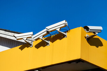 Four Security Cameras Mounted on a Bright Yellow Building Against Blue Sky