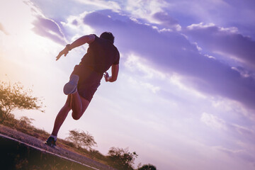 Silhouette of young man running sprinting on road. Fit runner fitness runner during outdoor workout with sunset background.
