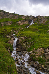 Waterfall flowing down mountain slopes along famous Grossglockner Hochalpenstrasse high mountain road in Austrian Alps. Road passes through Hohe Tauern National Park. Picturesque view.