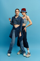 Twins showcase their unique style in matching denim outfits against a vibrant blue backdrop