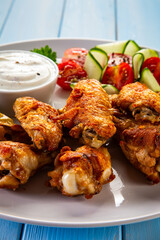 Baked chicken wings with white dressing and fresh salad on wooden table	