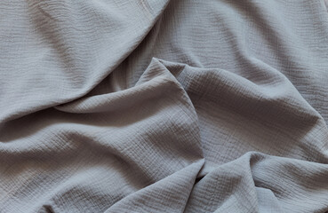 Fototapeta premium Top view of twisted gray cotton muslin fabric. Textile abstract background. Soft, comfortable, fashion material for sew and cutting. Sewing and needlework as a hobby. DIY concept. Flat lay, close-up