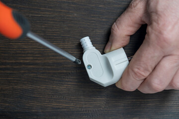 Using a Phillips screwdriver, loosen the screw on the white electrical power plug, closeup. The...