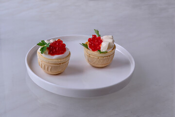 Tartlets with salmon caviar. Salmon caviar in waffle cups with boiled egg and mayonnaise. On white flat plate with rim and with parsley leaves