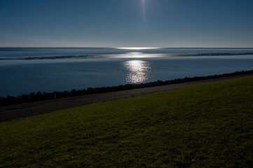 A serene coastal view on Schiermonnikoog, where the sun reflects on the calm sea, framed by a green embankment