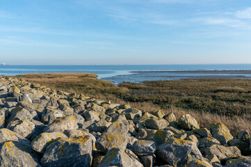 A serene view of the Schiermonnikoog coastline, featuring a rocky shoreline, tidal flats, and a blue sky