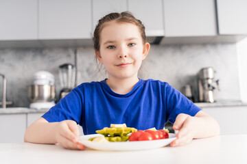 Cute girl sitting at the table with a healthy and delicious waffle breakfast with spinach, cheese and tomatoes. The concept of vitaminized nutrition for children. Selected focus.