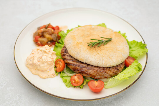 Serbian pljeskavica served with traditional Balkan side dishes. Balkan style pljeskavica burger on a plate