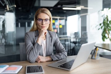 Portrait of serious confident female boss at workplace. Businesswoman looking at camera sitting at...