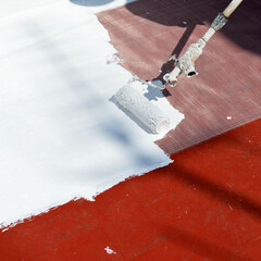 Pittura impermeabilizzante applicata a rullo per impermeabilizzare la terrazza di casa. Applicazione di pittura bianca sul tetto per contrastare il caldo estivo dovuto ai cambiamenti climatici.