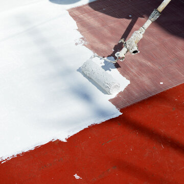 Pittura impermeabilizzante applicata a rullo per impermeabilizzare la terrazza di casa. Applicazione di pittura bianca sul tetto per contrastare il caldo estivo dovuto ai cambiamenti climatici.