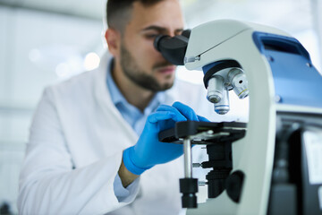 Close up of a male scientist  working on a medical research through a microscope in laboratory.	