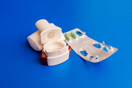 Inhaler and capsules with a medicine. COPD or Asthma capsule Inhaler on the blue isolated background. Inhaler or bronchodilator and medical powder capsules for prevention asthma.