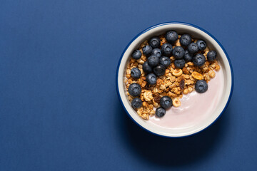 Bowl with blueberry greek yogurt and oat granola on blue background with copy space. Food breakfast background top view