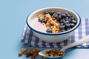 Bowl with blueberry greek yogurt and oat granola on light blue background with copy space. Food breakfast background top view