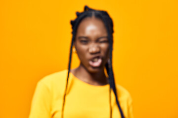 Young Black woman with braided hair expressing joy and playfulness against a vibrant yellow background, ideal for joyful themes, emotions, and lifestyle concepts