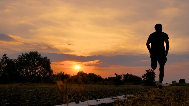 Silhouette of young man running sprinting on road. Fit runner fitness runner during outdoor workout. 4K
