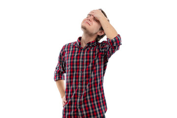 A young man in a plaid shirt holding his forehead with a thoughtful expression against a white...