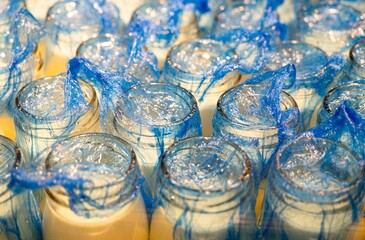 Close-up of freshly made pudding in jars covered with blue wrap. 