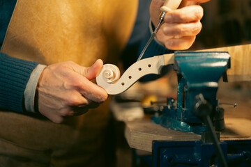 Luthier carefully carving violin scroll in workshop