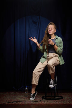 Young woman delivering standup comedy performance on stage with a microphone in hand, exuding confidence and engaging with audience