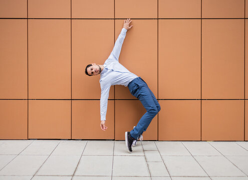 Cuban dancer leans dynamically against a brown wall