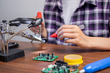 Close up of technician young woman repair electronic circuit board with soldering iron and tin wire on the table.