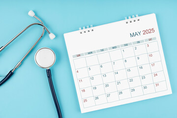 May 2025 desk calendar and stethoscope on blue, Medical appointment concept.