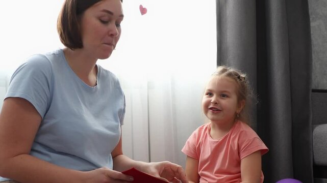 Mid shot of young Caucasian woman speech therapist reads a book with a cute girl. Preschool education for young children.