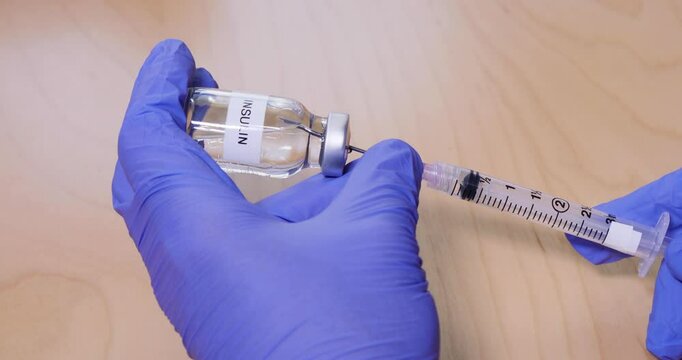 A nurse or doctor uses a syringe to draw up insulin from a vial.  	