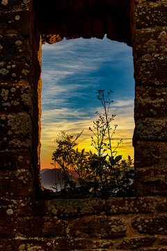 Window to the sky. On a castle ruin I discovered an old window covered with grass through which the sunset can be seen. It looks like a picture frame made of stone