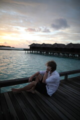 Fototapeta premium young man sitting on a pier at sunset