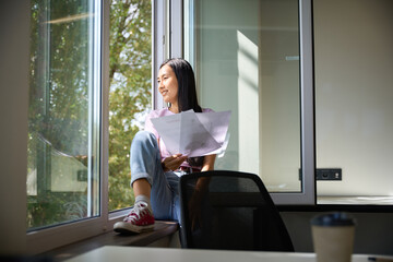 Beautiful woman is sitting with project documentation on the windowsill
