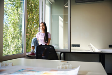 Freelancer woman is sitting on the windowsill of a large window