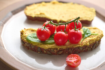 Close up shot of hummus on wholegrain bread with cherry tomatoes and basil. Helthy food concept