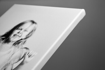 Angled close-up of a black and white photo canvas print featuring a smiling girl, with a tightly stretched gallery wrap edge, against a gray background