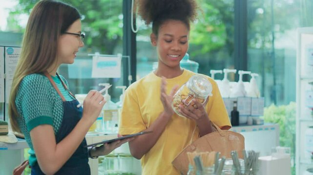 Shopkeeper describes natural organic products to woman customer in refill store, zero-waste and plastic-free grocery, eco environment-friendly, sustainable lifestyles with a reusable shop.