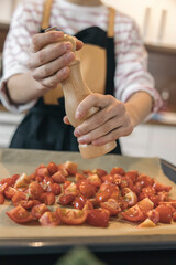 Unrecognizable girl seasoning chopped tomatoes with pepper mill, preparing ingredients for cooking