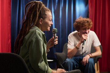 Two people engaging in an animated podcast conversation in recording studio setting. They are focusing on delivering an engaging discussion for their audience