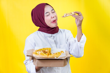 A joyful asian woman savoring pizza against a bright yellow backdrop, showcasing her love for food.